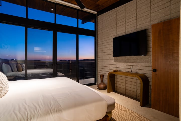 Bed facing the glass, the hills beyond